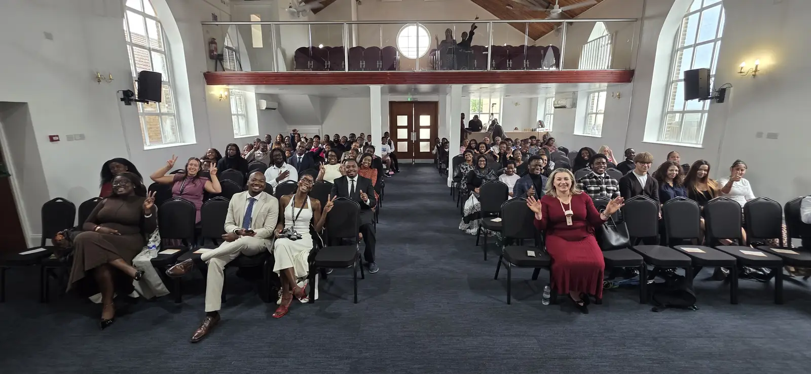 The congregation seated in the main hall, smiling towards the camera